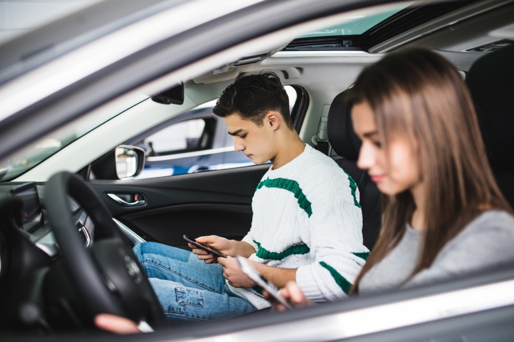 Two teens in a car, one driving, both texting