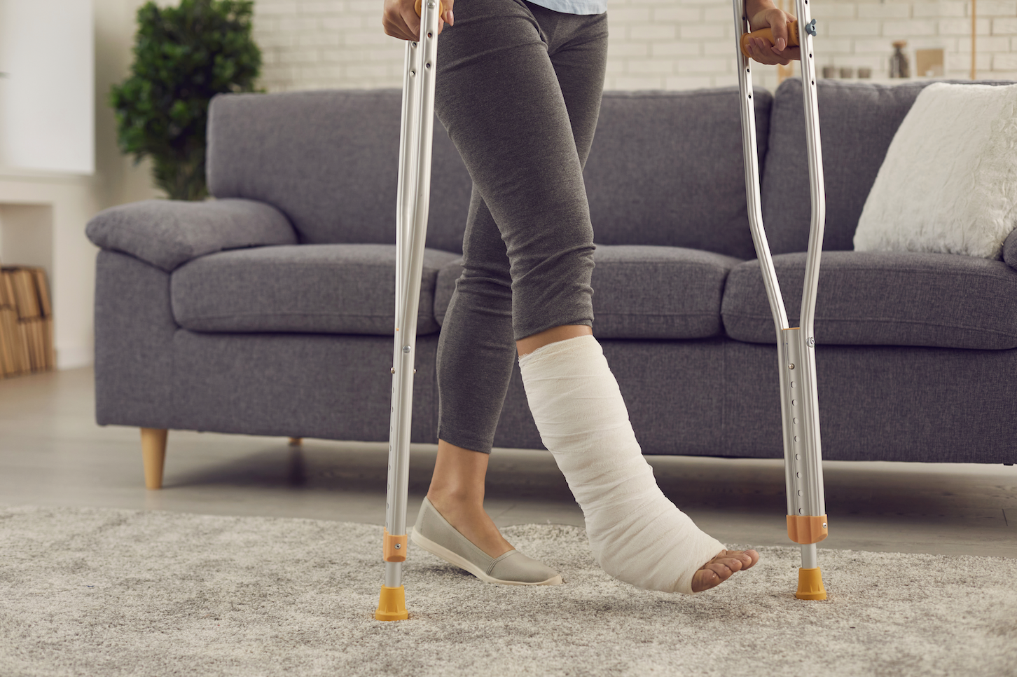 leg injury cast woman in a cast on crutches in front of her couch