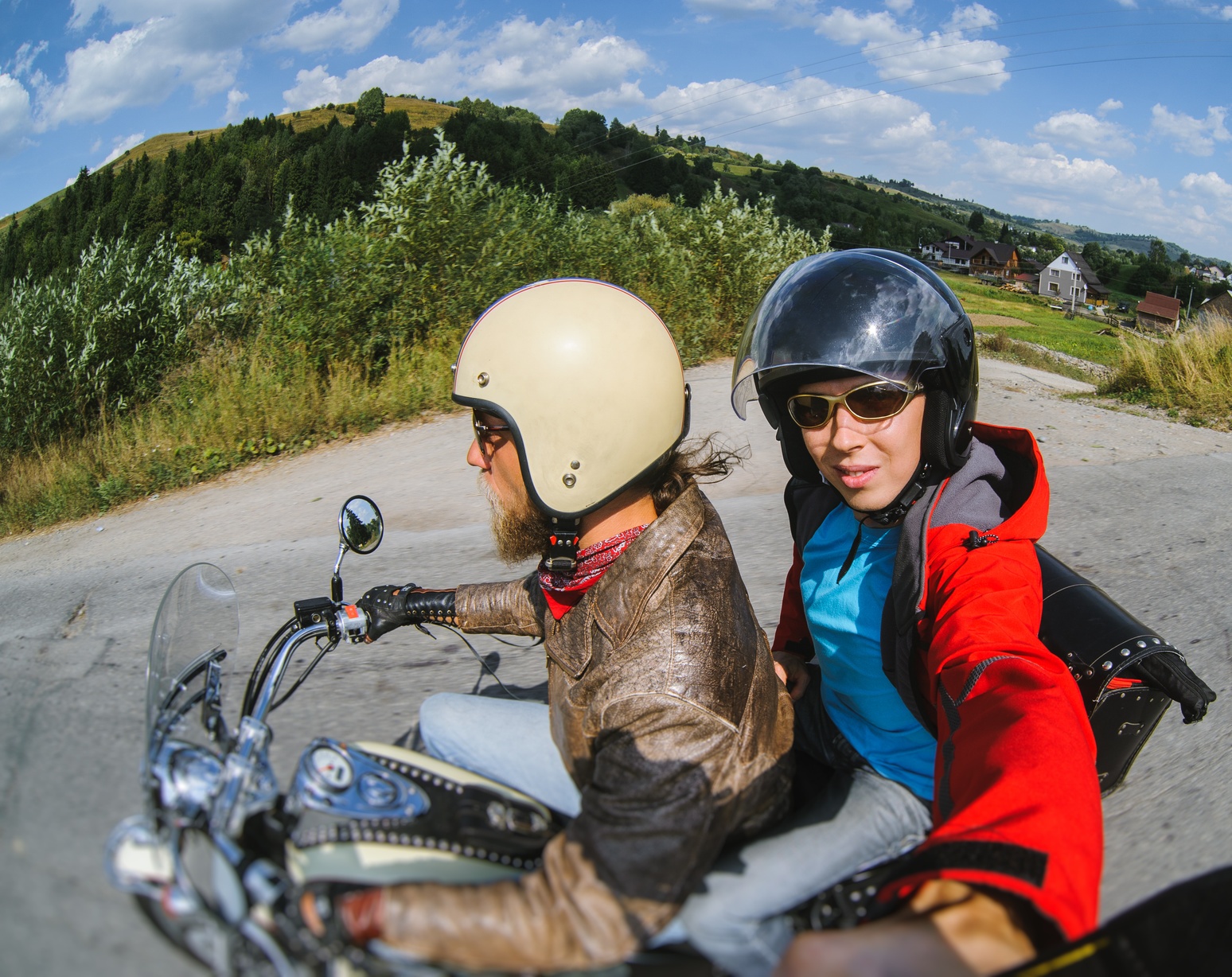 A couple riding a motorcycle, the passenger taking a selfie with selfie stick.
