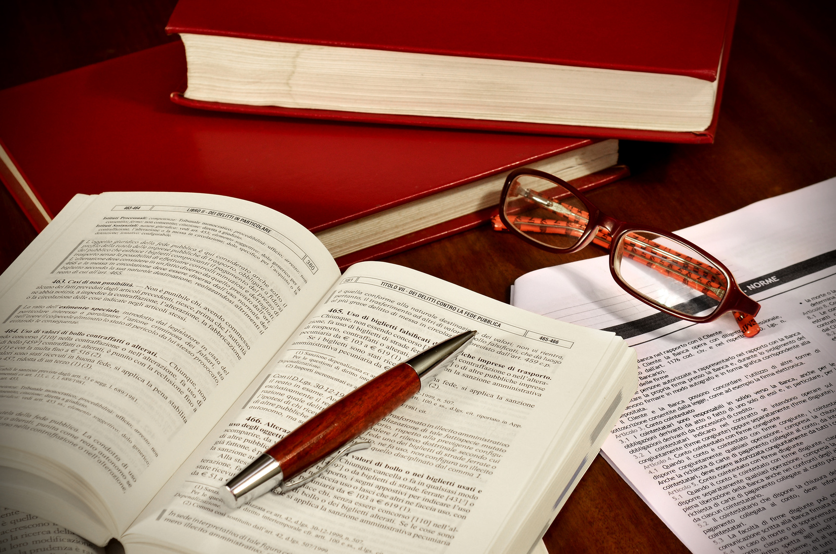 Libri di diritto e codici di legge per avvocato A stack of books, one book open, a pair of glasses and some documents on a desk
