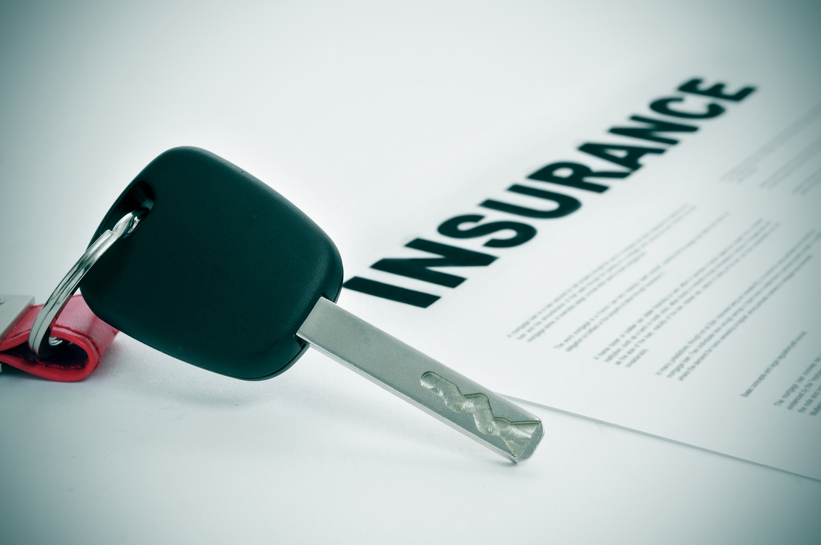 car insurance closeup of a car key and a insurance policy on a white surface