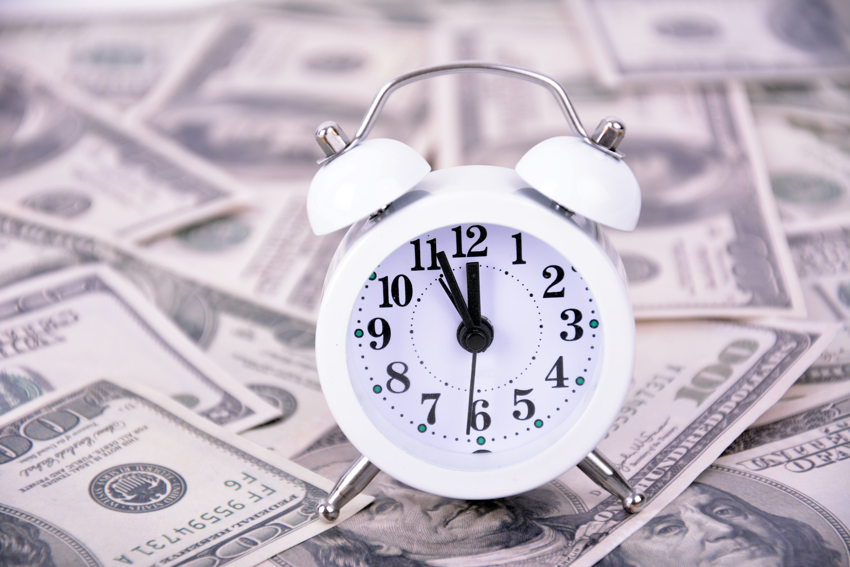 Para An alarm clock on a table covered in hundred dollar bills