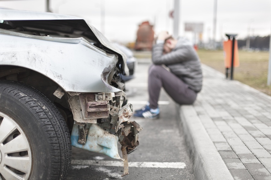 top-3-questions-to-ask-after-an-auto-accident Man sitting on curb holding back of head after being in a car accident